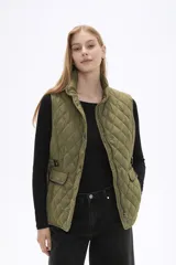 Chaleco acolchado de diseño capitoneado en color verde militar, con cuello alto, cierre frontal con cremallera y botones a presión. Presenta bolsillos frontales con solapa y detalles de ribetes en tono contrastante.