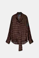 Camisa de seda con estampado tipo pañuelo en tonos marrones y ocres, cuello solapa, manga larga y detalle de pañuelo integrado en el cuello. Presenta bajo asimétrico y cierre frontal con botones.