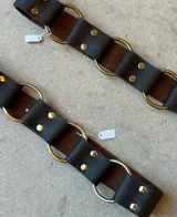 Cinturón de cuero marrón con diseño de argollas metálicas unidas por piezas de cuero sujetas con remaches dorados.