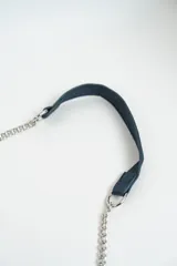 Cartera de hombro color azul marino, con solapa frontal decorada con tachas en forma de estrellas plateadas. Los bordes están adornados con un detalle de cadena entrelazada y la correa es una combinación de cadena plateada y una sección de cuero sintético.