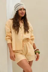 Camisa amarilla de manga larga con diseño de rayas finas, corte oversize, cuello camisero, cierre frontal con botones y bolsillo ojal en el pecho.