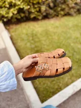 Sandalias suecos color camel con tiras de cuero trenzado, hebilla metálica y suela de goma negra.