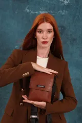 Phonebag pequeña color mostaza, confeccionada en cuero sintético, con solapa frontal y correa ajustable con logo de la marca.