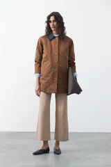 Trench tipo barn jacket color marrón, con cuello camisero en contraste azul marino, cierre frontal con broches y bolsillos amplios. De silueta recta y calce cómodo.