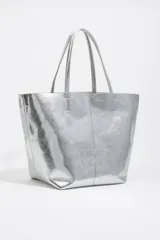 Bolso shopper de tamaño grande confeccionado en cuero reciclado con acabado metalizado plateado. Presenta doble asa superior, costura central vertical y logo de la marca bordado en el frente. Incluye cierre de mosquetón y bolsillo interior.
