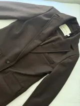 Tapado de lana color bordó con solapas y detalles en los bolsillos de cuero. Presenta cierre frontal con botones y diseño de líneas clásicas.