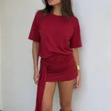 Vestido corto rojo de manga corta con hombreras, diseño holgado en la parte superior y falda drapeada ajustada con un detalle de anudado lateral y larga tira colgante.