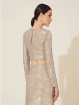 Blusa corta dorada cubierta de lentejuelas, de mangas largas y cuello redondo.