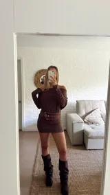 Vestido corto de punto color marrón, con escote tipo bote que deja los hombros al descubierto y mangas largas. El diseño es ajustado al cuerpo.