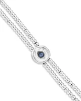 Pulsera de doble cadena formada por pequeñas esferas metálicas bañadas en plata, con un dije central circular en forma de ojo que contiene un cristal azul en el centro.