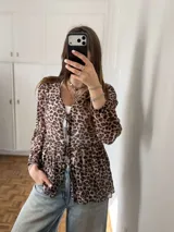 Blusa de manga larga con estampado animal print tipo leopardo, corte holgado con diseño peplum y cierre delantero mediante finos cordones para ajustar.
