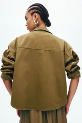 Campera camisera de sarga de algodón color verde militar, con cuello clásico, cierre frontal de botones metálicos, canesú y bolsillos de parche delanteros.