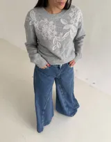 Sweater de punto color beige con cuello redondo, manga larga y detalle de bordado floral en la parte superior del pecho.