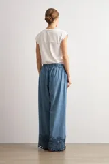 Pantalón de jean de corte holgado y pernera ancha, con cintura elástica y detalle de bordado oscuro con diseño floral y perforaciones en el bajo.