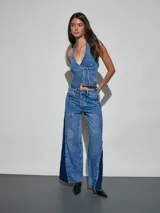 Chaleco de denim azul de corte ajustado, con escote halter pronunciado, detalle de tachas metálicas en los bordes y cierre delantero con tiras para anudar.