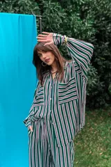 Conjunto de camisa y pantalón de fibrana con diseño a rayas verticales en tonos verde, blanco, violeta y negro. La camisa es de corte amplio con bolsillos frontales en el pecho, y el pantalón es de corte recto y holgado.