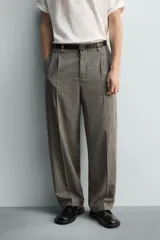 Pantalón de corte relajado con diseño de cuadros, confeccionado en tejido con lana. Presenta cintura con pliegues frontales, bolsillos laterales y bolsillos traseros de vivo, con cierre frontal de cremallera y gancho metálico oculto.