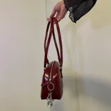 Bolso tipo baguette negro de cuero sintético con doble asa corta y cierre superior con cremallera.