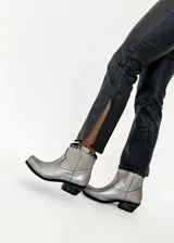 Botas texanas plateadas de cuero vacuno, con caña corta, taco bajo y detalle de tiento cosido a mano en la parte superior.