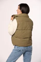 Chaleco puffer de nylon en color verde oliva, con cuello alto, cierre frontal con cremallera y botones a presión, y bolsillos laterales.