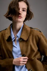 Chaqueta corta de efecto ante en color marrón, con cuello solapa, manga larga y trabillas en los hombros. Presenta cierre frontal con botones y bolsillos delanteros de doble vivo.
