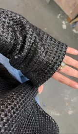 Blusa negra metalizada con escote bote que puede usarse recto o caído en un hombro y mangas largas acampanadas.