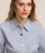 Vestido corto chemise de algodón con estampa a rayas celestes y blancas, cuello solapa, manga larga, abotonado frontal y cintura marcada con falda evasé con pliegues.