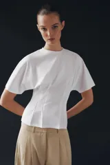 Camiseta de algodón con cuello redondo y manga corta. Presenta un diseño entallado con pinzas en la cintura y bajo recto.