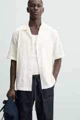 Camisa de corte relajado confeccionada en tejido de algodón con diseño jacquard floral. Presenta cuello bowling, manga corta, un bolsillo de parche en el pecho y aberturas laterales en el bajo. Cierre frontal con botones al tono.