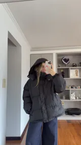 Campera puffer de corte holgado en color beige, con diseño acolchado, cuello alto y capucha desmontable. Cuenta con cierre frontal y botones a presión, además de puños elásticos.