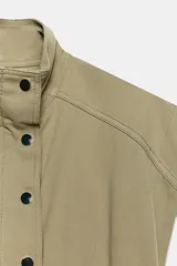Chaleco de cuello alto y manga sisa, color verde militar, con elásticos fruncidos en la cintura y cierre frontal de botones metálicos a presión.