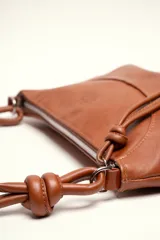 Cartera bandolera de cuero marrón con forma relajada, diseño de costuras curvas y detalles de nudos hechos a mano en las asas.