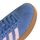 Championes Adidas VL Court 3.0 de estilo urbano, confeccionados en gamuza sintética color azul con las icónicas tres tiras laterales en color rosado. Presentan una suela de goma color caramelo y un diseño inspirado en el calzado retro de canchas.