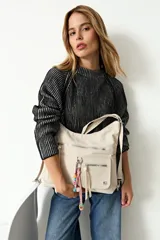 Bolso tipo hobo convertible a mochila, color beige, con múltiples bolsillos frontales con cierre metálico y llavero decorativo multicolor removible. Cuenta con correa regulable.