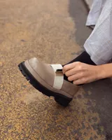 Mocasines de cuero color beige con suela track negra de goma y detalle de banda elástica blanca sobre el empeine.