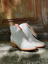 Botas cortas de cuero sintético color beige con detalles de costuras estilo western.