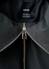 Chaqueta estilo bomber color negro, de corte oversize, con cuello alto amplio, cierre frontal de cremallera metálica y bolsillos laterales.