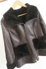 Campera reversible de cuero genuino napalán color marrón oscuro, con cuello, solapas, bolsillos frontales y detalles en corderito negro. Cierre frontal con cremallera.
