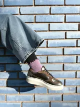 Zapatillas deportivas de cuero color peltre, con cordones negros y suela de goma blanca.