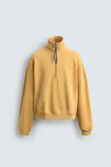 Sudadera de corte relajado confeccionada en algodón con interior de rizo, color amarillo mostaza con efecto lavado. Presenta cuello subido con cierre frontal de cremallera y detalle de cinta trenzada en el tirador, manga larga y acabados en rib.