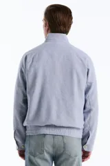Campera estilo Harrington de corte clásico con diseño de rayas finas verticales en tono celeste y blanco. Cuenta con cuello alto, cierre frontal completo, bolsillos diagonales con solapa y botones, además de puños y dobladillo elastizados. Presenta el logo bordado del pingüino característico en el pecho.
