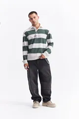 Polo de manga larga con diseño de rayas horizontales en color verde y blanco. Presenta cuello camisero, cartera de botones y estampado frontal con texto.