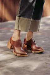 Zapato de cuero color beige, con taco de madera y suela dentada. Presenta un diseño slip-on con detalles de textura en relieve en los laterales y el empeine.