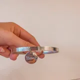 Pulsera rígida plateada con dije circular colgante con la palabra "Victoria" grabada.