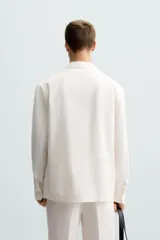 Blazer color blanco confeccionado en tejido con mezcla de algodón y lino, de corte recto y holgado. Tiene cuello con solapas de muesca, manga larga con puños abotonados, bolsillos frontales de parche y cierre frontal con botones.