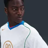 Camiseta deportiva Nike Total 90 Energy de manga corta, color blanco con detalles en dorado, verde, azul y rojo. Presenta un diseño de paneles curvos, cuello en V tricolor y el gráfico distintivo '90' en el centro del pecho.