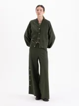 Pantalón de corte recto y silueta holgada, confeccionado en tejido rústico de algodón color verde militar. Presenta cintura con elástico interno y detalles de broches metálicos a presión en los laterales.