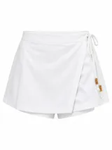 Short pollera blanco de tiro alto, confeccionado en símil lino, con diseño cruzado tipo falda en el frente y detalle de lazos con cuentas de madera en el lateral.