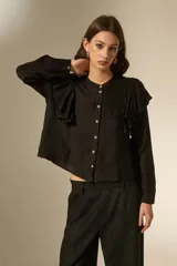 Camisa negra de viscosa con textura arrugada, cuello a la base y cierre frontal con botones. Presenta volados en los hombros y mangas largas.
