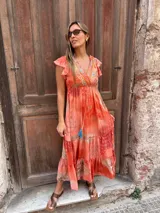Vestido largo color naranja con estampado en tonos rojos y turquesas, escote en V cruzado con detalles bordados, mangas cortas con volados, cordón ajustable en la cintura y falda escalonada.